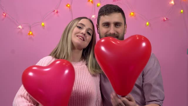 一个相爱的男人和一个女人拿着心形的气球看着你。情人节视频素材