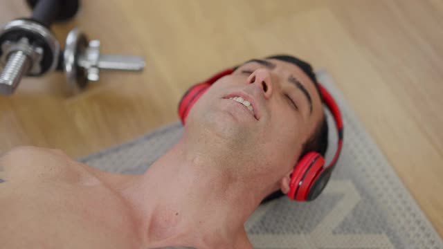 一个放松的中东运动员在训练后戴着耳机听音乐。特写自信疲惫的运动员休息后，室内锻炼。男子气概和运动。视频下载