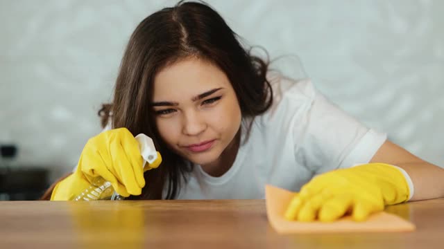 年轻妇女打扫家里。一个黑发的女模特正在厨房里清理一个灶台。女孩在打扫公寓里的灰尘视频素材