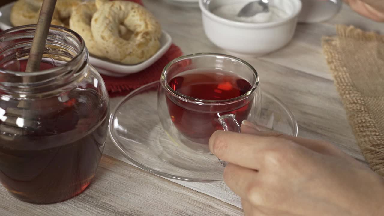 高角度特写的女人的手搅拌在一个白色质朴的桌子上的杯子木槿热茶视频素材