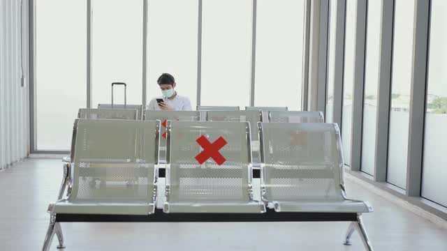 亚洲年轻男女游客戴着防护卫生口罩，在机场坐着社交距离椅。视频素材