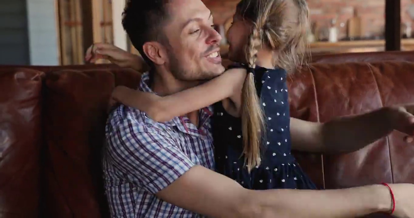 快乐的爸爸，他的女儿紧紧拥抱坐在沙发室内视频素材