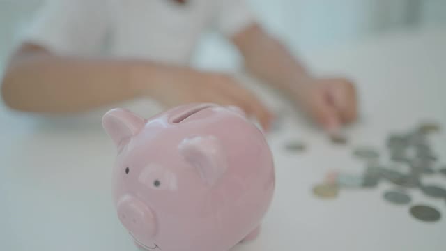 亚洲学前班的小男孩在家里的客厅里存钱，把硬币放进扑满，为自己的未来做准备。视频下载
