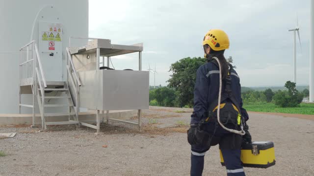 亚洲妇女检查工程师戴着安全带和安全线在泰国风电场准备和检查风力发电机的安全。视频下载