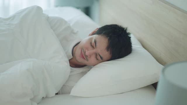 亚洲男人睡甜蜜的梦在一个舒适的午睡在床上在房子里的卧室视频素材
