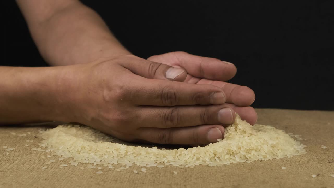 一名农民正在铲米粒。干种子从那人的手中溢出来。视频下载