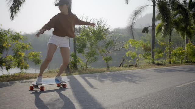 亚洲妇女在美丽的夏天在户外冲浪或滑冰。快乐的年轻女子早上在公园玩冲浪滑冰。体育活动生活方式概念。视频下载