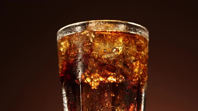 可乐杯与冰块缓慢旋转特写。冷饮在棕色背景下旋转。4 k视频视频素材