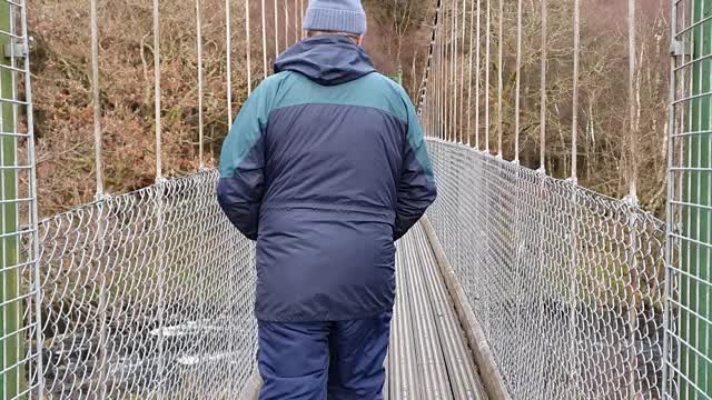 一名男子在迪夫河上的吊桥上行走，苏格兰肯敦视频下载