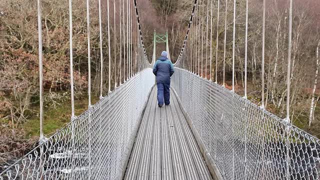 在苏格兰，一个人走着，看着下面的河上的吊桥视频下载