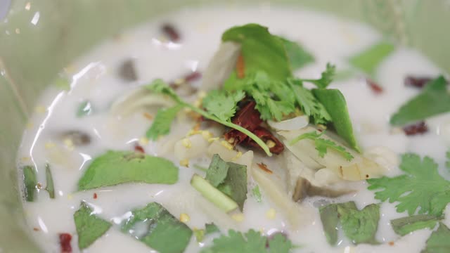 泰国椰奶汤与鸡肉和蘑菇在绿色陶瓷碗的特写。视频下载