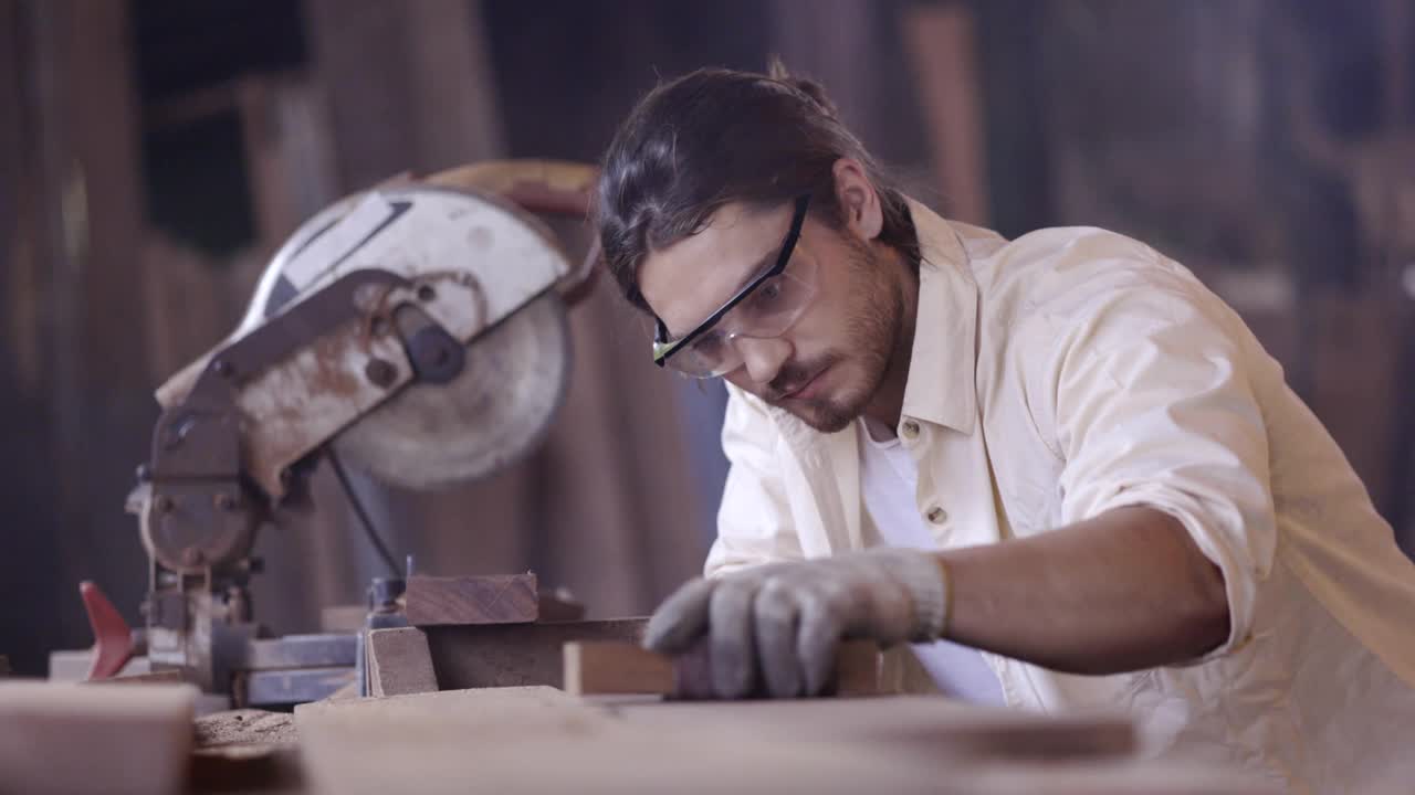 白种人木匠，在木家具厂工作，使用木砂和机器或电动木锯。工作时戴安全手套和眼镜。产品质量检验服务视频素材