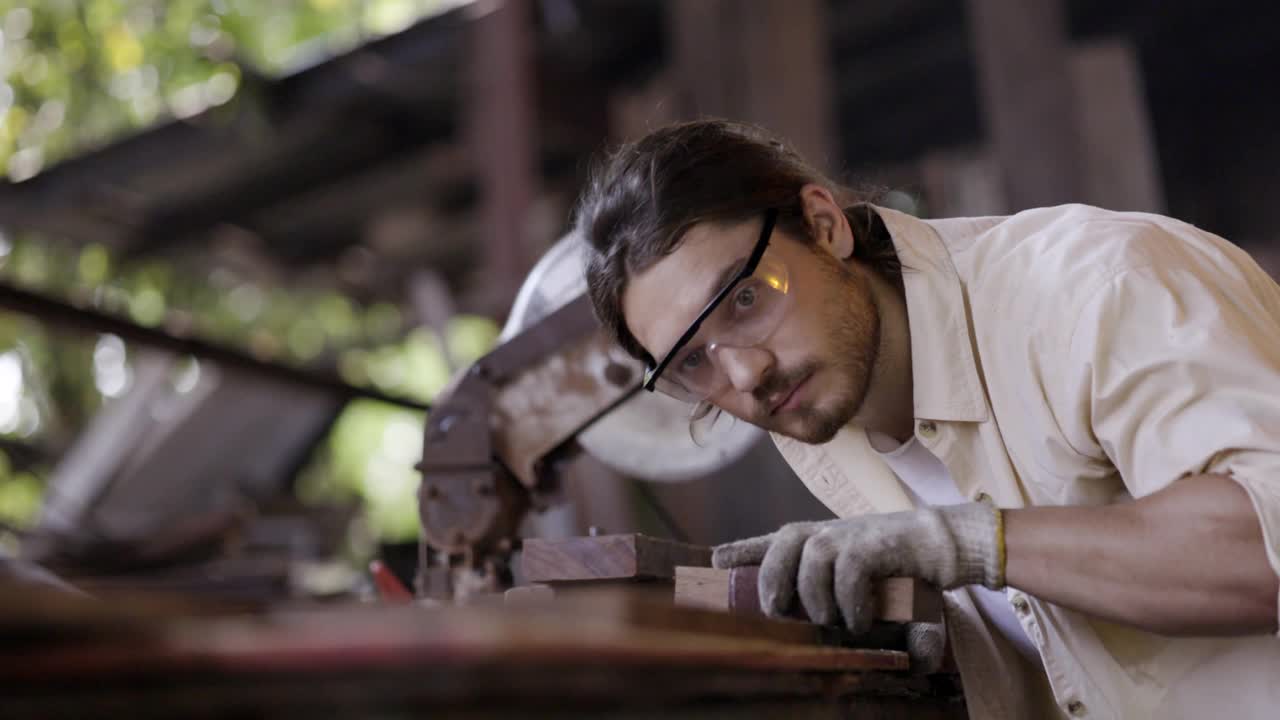 白种人木匠，在木家具厂工作，使用木砂和机器或电动木锯。工作时戴安全手套和眼镜。产品质量检验服务视频素材