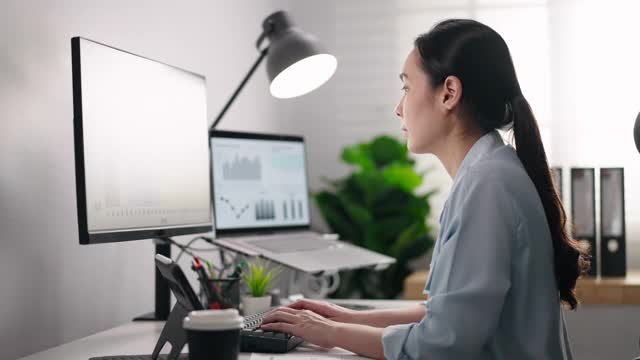 在一个被数据电脑屏幕包围的办公室里工作的亚洲女商人视频素材