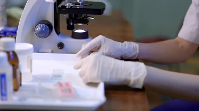 女性微生物学家戴上防护面罩，将载玻片置于显微镜下视频下载
