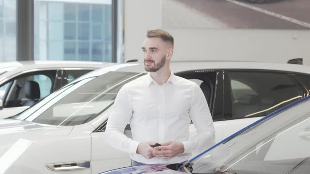 英俊快乐的男人对着镜头微笑站在汽车经销商视频下载