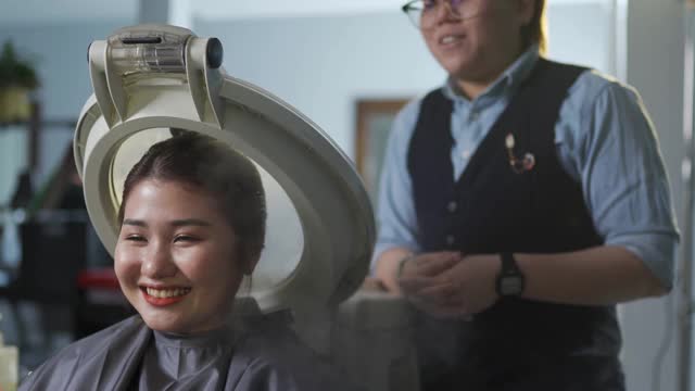 一名亚裔华裔女性在美发厅接受头发蒸润护理，并与发型师交谈视频下载