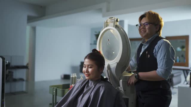一名亚裔华裔女性在美发厅接受头发蒸润护理，并与发型师交谈视频素材