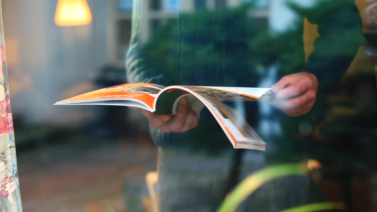 在一间自我隔离的房子里，一名男子在窗前翻阅一本杂志视频下载