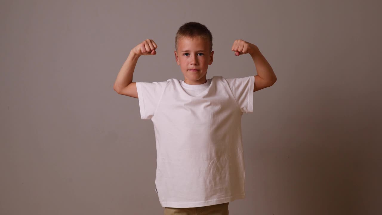 那男孩露出手臂上的肌肉。强壮的男孩。在一吨重的背景上穿着白色t恤的孩子视频下载