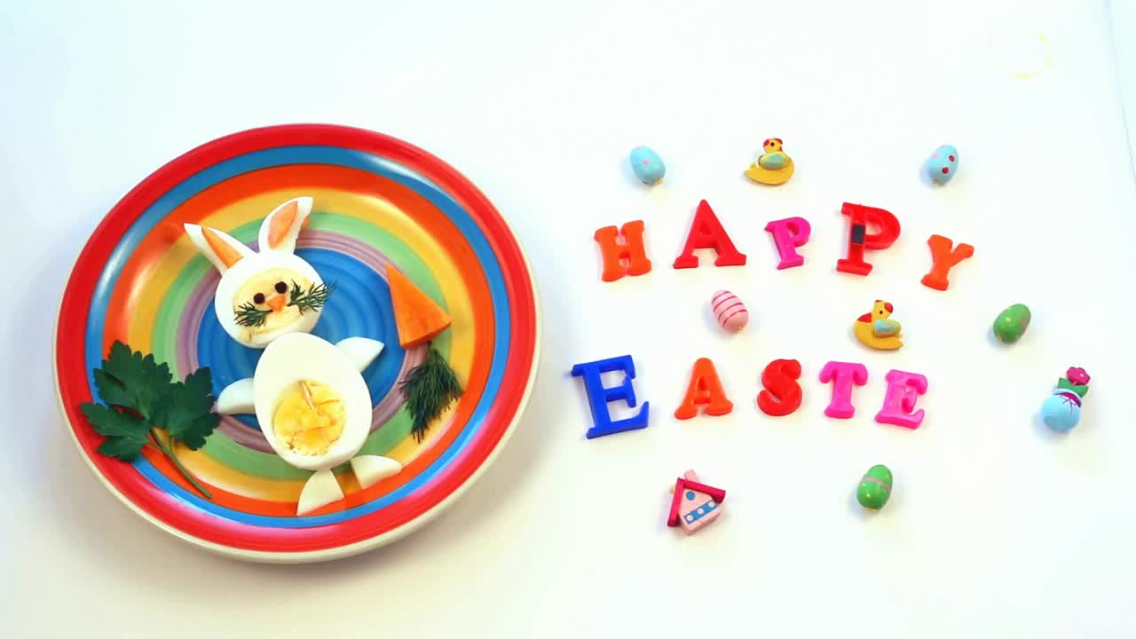 给孩子们的复活节早餐点子。兔子蛋做成的兔子兔子彩盘上，白色背景，题字复活节快乐，俯视图视频下载