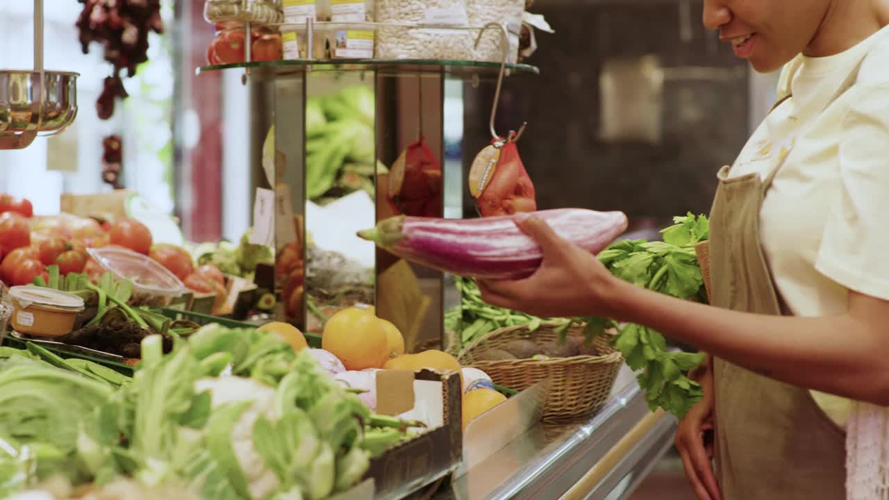 微笑的女人在市场的摊位上买新鲜的茄子视频下载