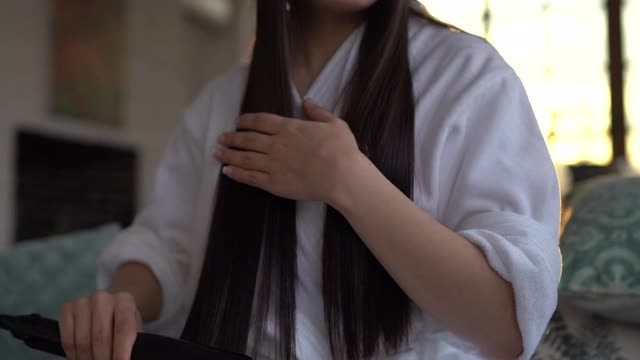 穿着浴袍的年轻女子正在用电熨斗烫头发视频下载