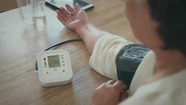 一位老年妇女正在家中用数字压力表测量自己的血压和心率。视频素材