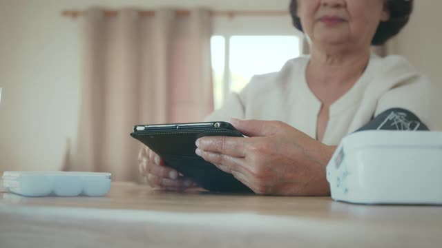 老年妇女自己用数字压力表测量血压和心率，并在家里用平板记录测试结果。视频下载