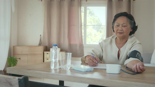 老年妇女自己用数字压力表测量血压和心率，并在家里用纸记录测试结果。视频下载