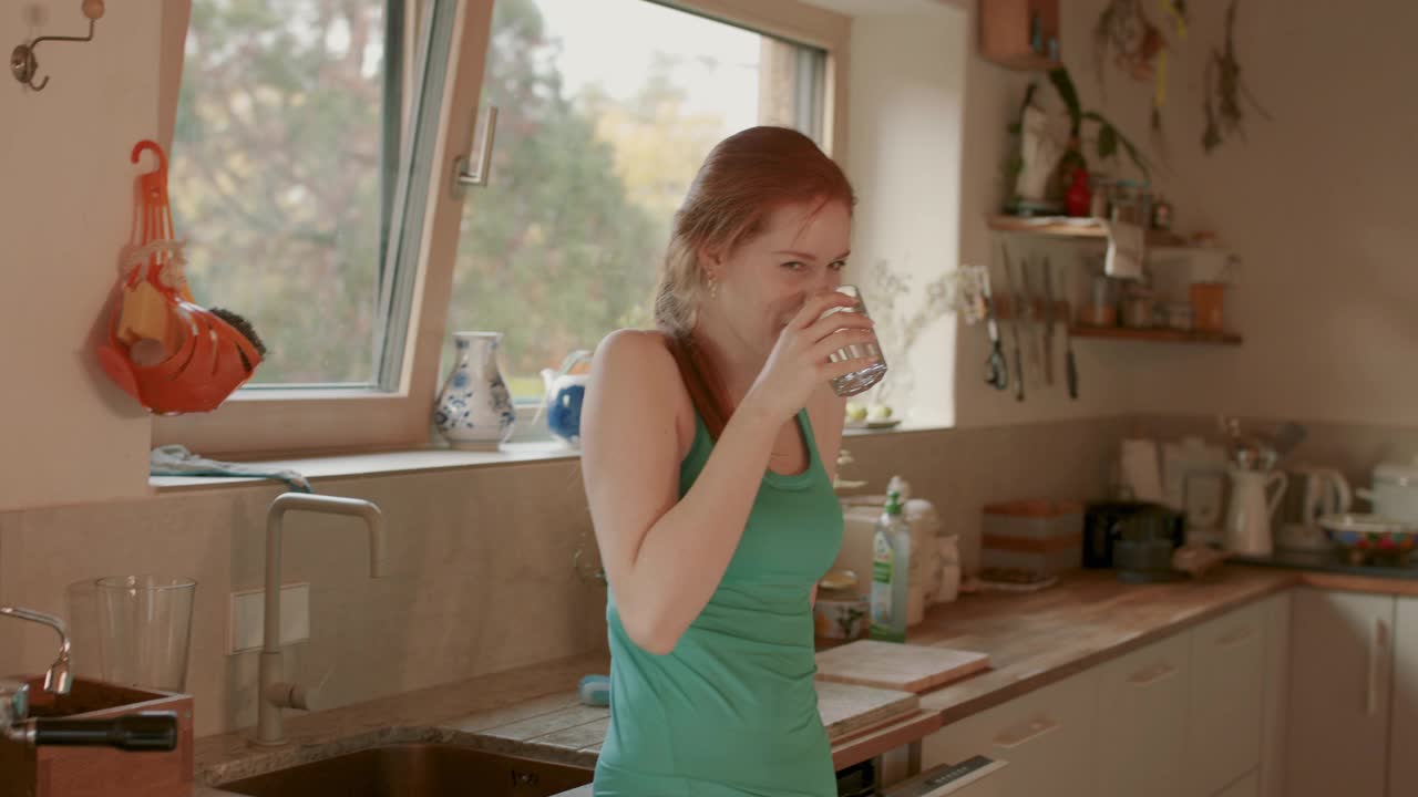 年轻女子在厨房里喝着一杯水视频下载