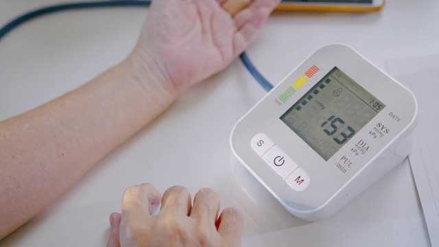 老年妇女在家用医疗器械手检查血压和心率。视频下载