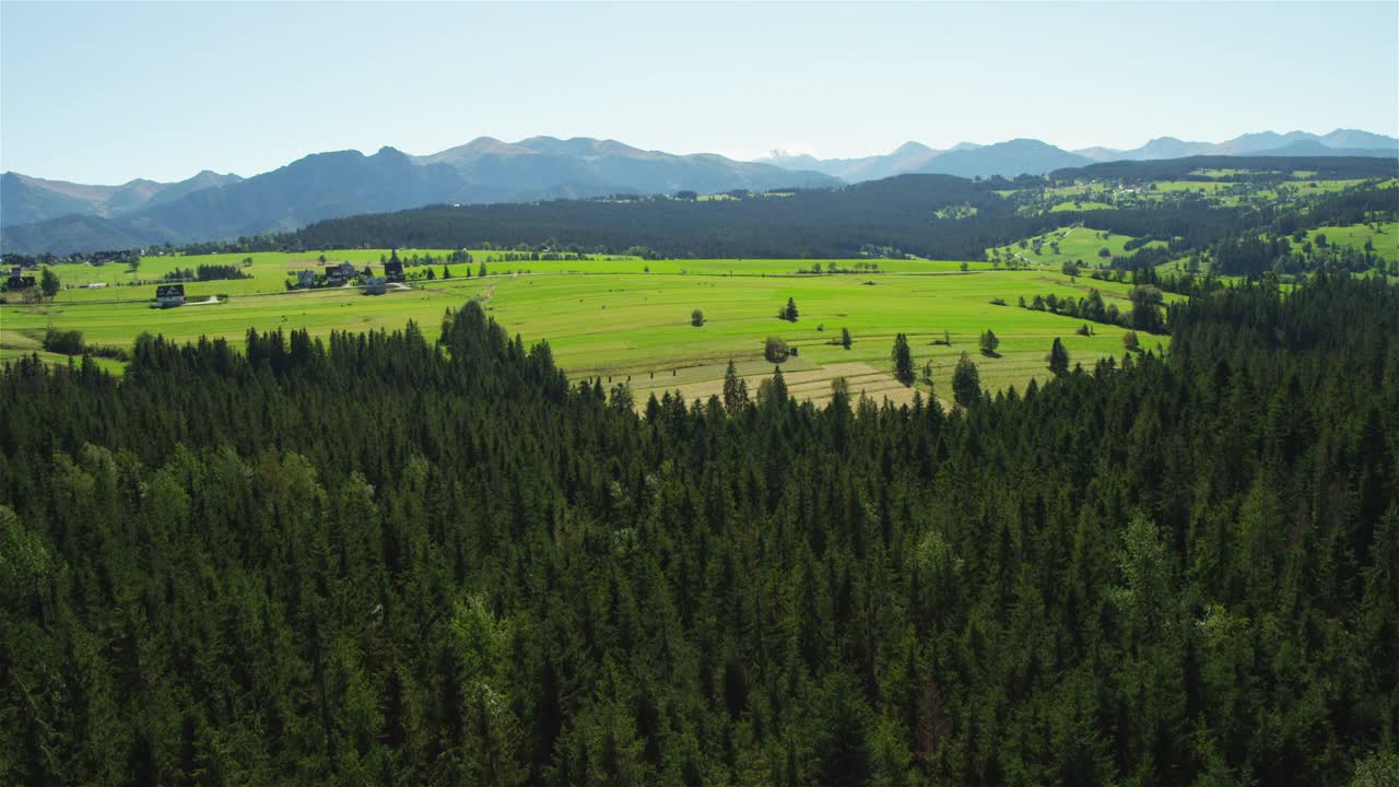 在一个阳光明媚的日子里，绿色的山丘和遥远的塔特拉山脉。无人机的观点视频下载