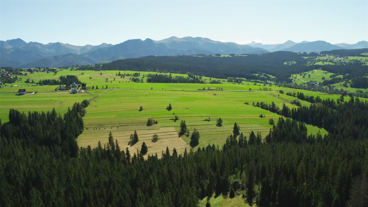在一个阳光明媚的日子里，绿色的山丘和遥远的塔特拉山脉。无人机的观点视频下载