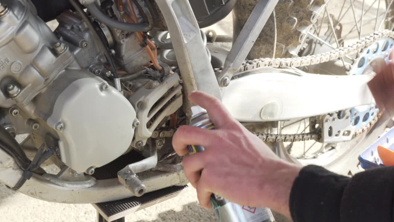 一名男子在给一辆越野摩托车的链条上油视频下载