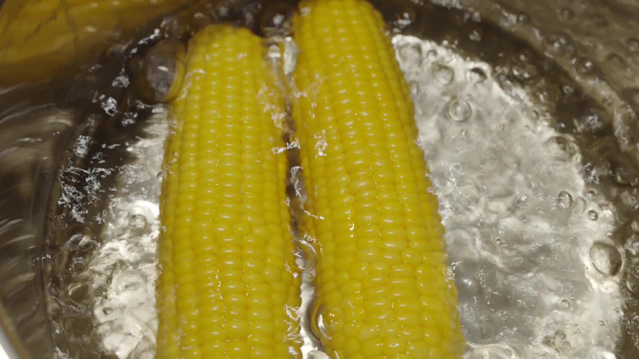 缓慢的运动。熟透的玉米穗放在沸水里，以增进健康。热锅里的黄色玉米。俯视图视频素材