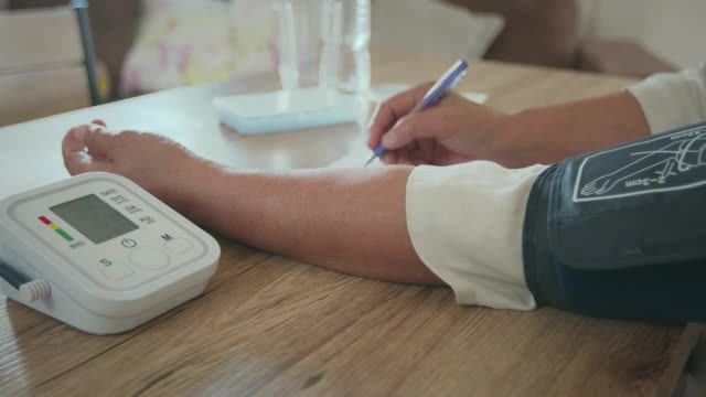 老年妇女自己用数字压力表测量血压和心率，并在家里用纸记录测试结果。视频下载