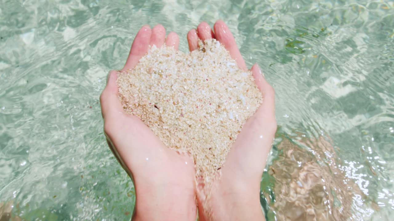 女孩的双手展示着来自大海的珊瑚沙。慢镜头，假日背景视频素材