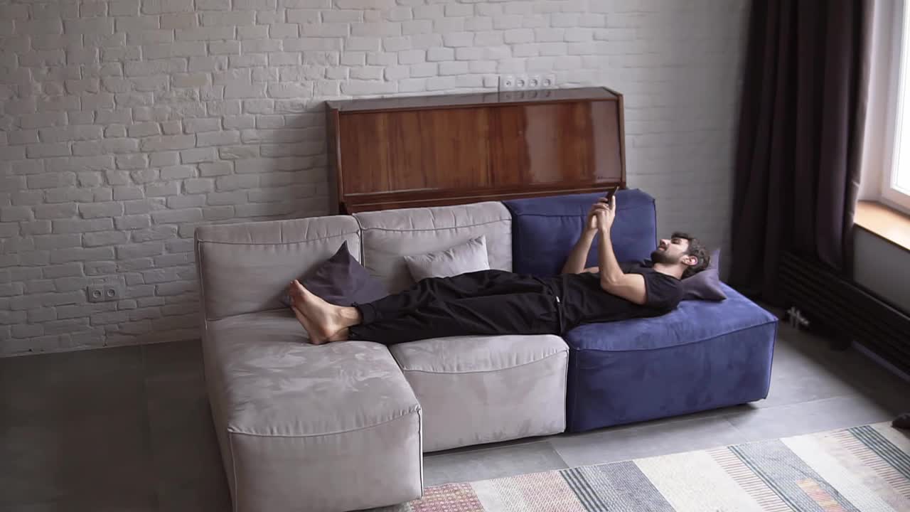 男人躺在沙发上用智能手机，滚动各种手势，比如滑动和滚动视频下载