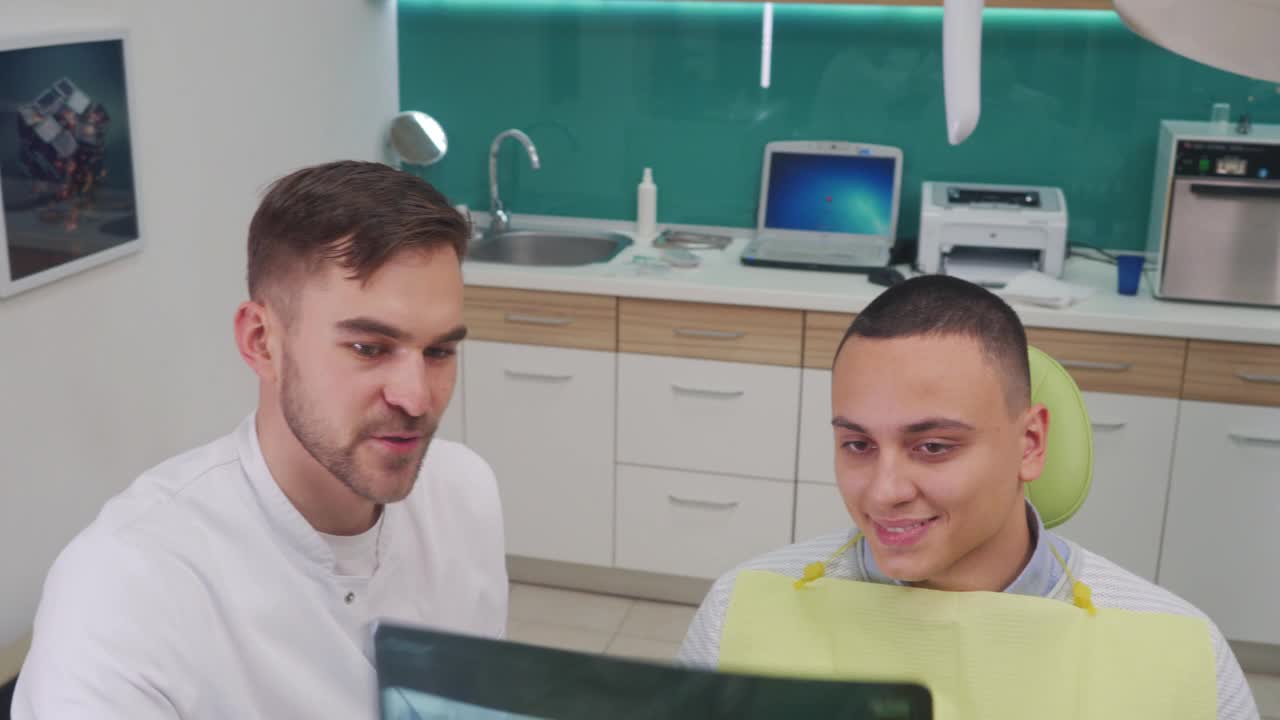 骄傲的牙齿矫正医生向他的病人展示了他的牙齿的x光图像，在他们成功地解决了覆盖牙齿的问题视频下载