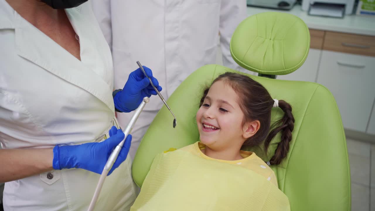 女牙医用一个有角度的镜子和牙钻修复小女孩乳牙上的蛀牙视频素材