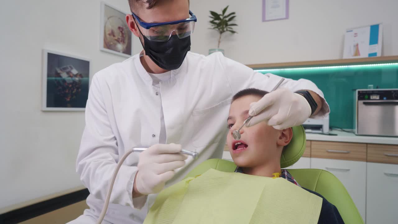 男性牙医修复牙齿上的蛀牙，同时使用有角度的镜子和牙钻视频下载