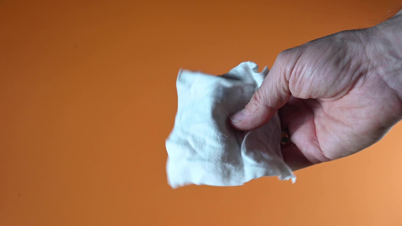 男人的手挤压湿纸巾，水就出来了。橙色背景。视频下载