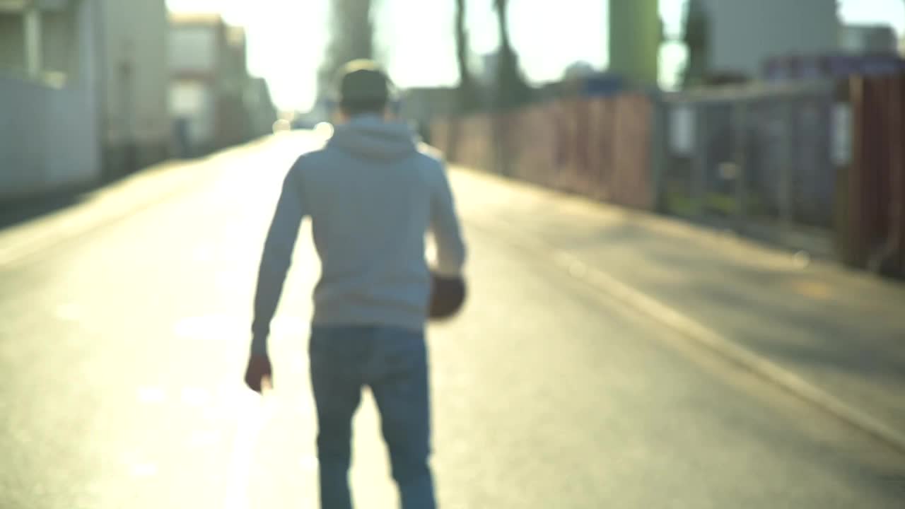 一个年轻人拿着篮球和耳机走在街上视频下载