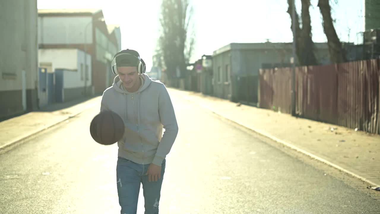 一个年轻人拿着篮球和耳机走在街上视频下载