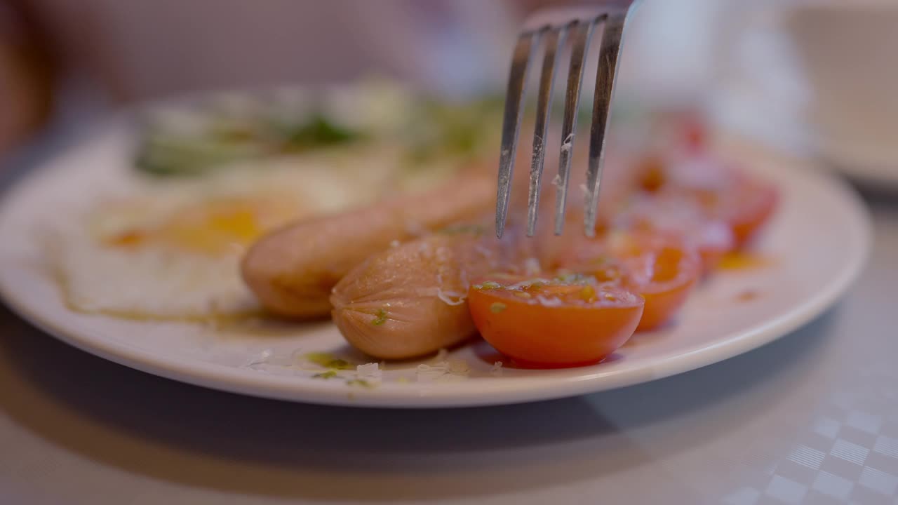 用叉子戳西红柿的特写，配上英式早餐。一个面目全非的人在餐厅或咖啡馆用餐。营养和节食概念。视频素材