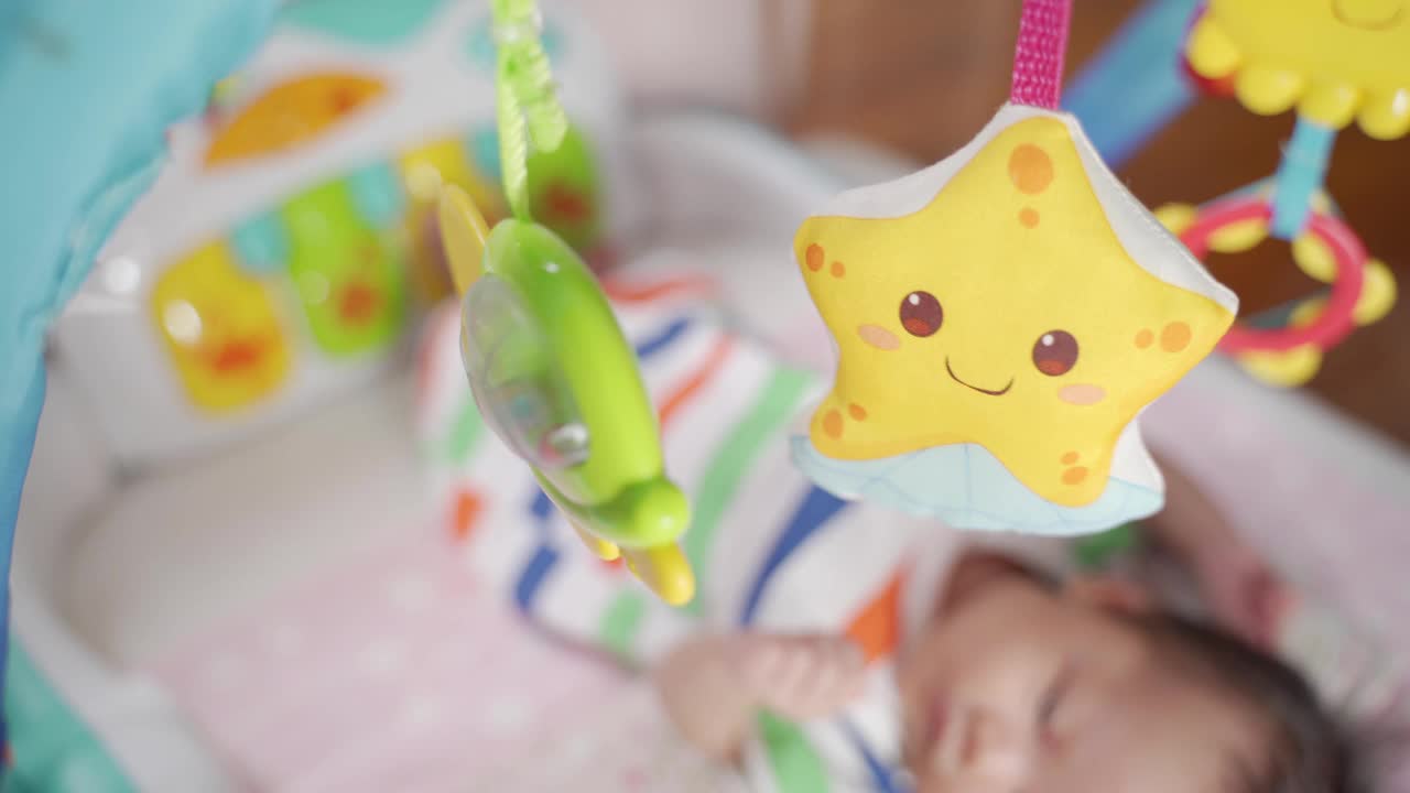 亚洲婴儿在多彩的体操垫子上玩耍提高技能。为支持新生儿发育而设计的运动馆。在婴儿床上挂移动玩具。视频下载