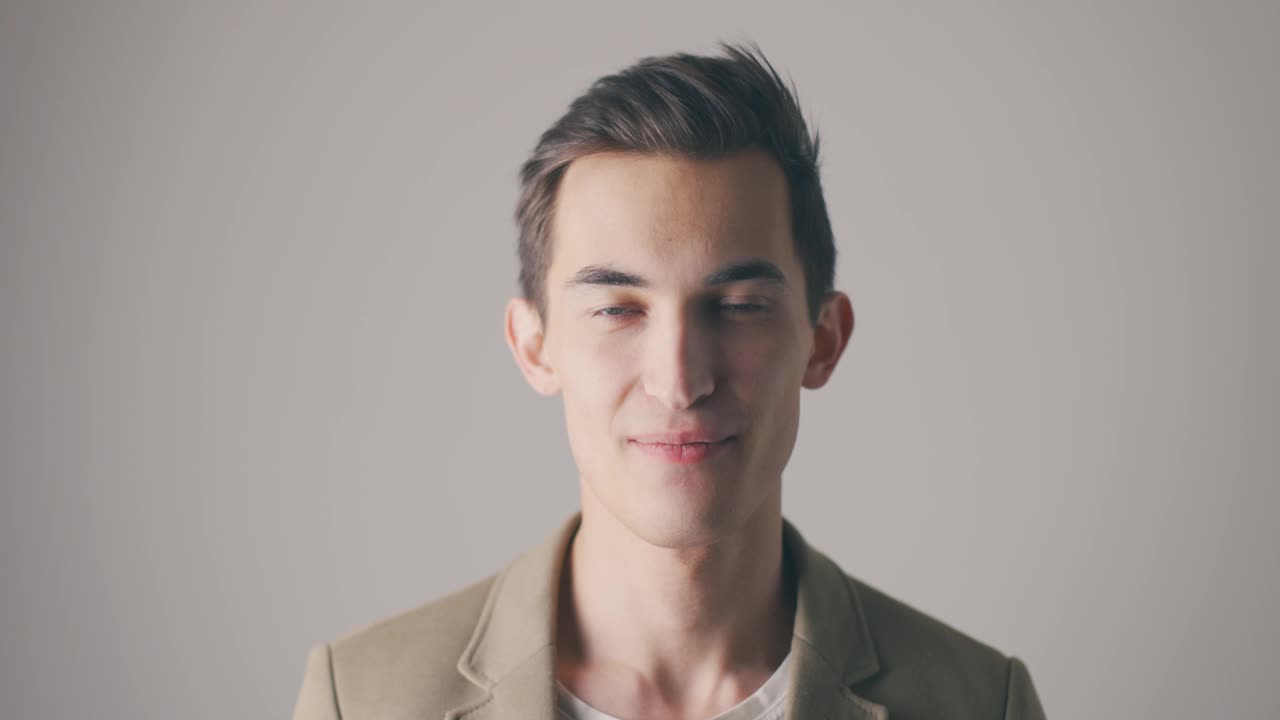 快乐微笑的年轻白人男子的肖像在灰色的背景在工作室视频素材