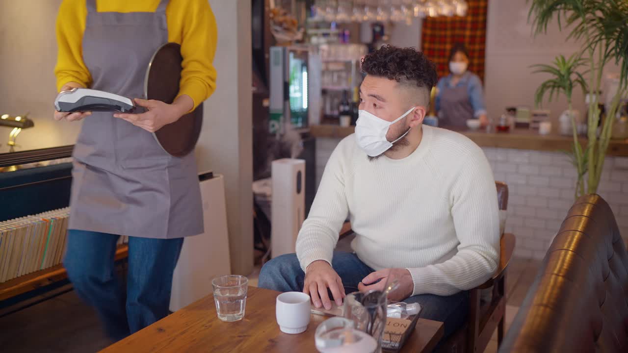 佩戴防护口罩的年轻人在café进行非接触支付视频素材