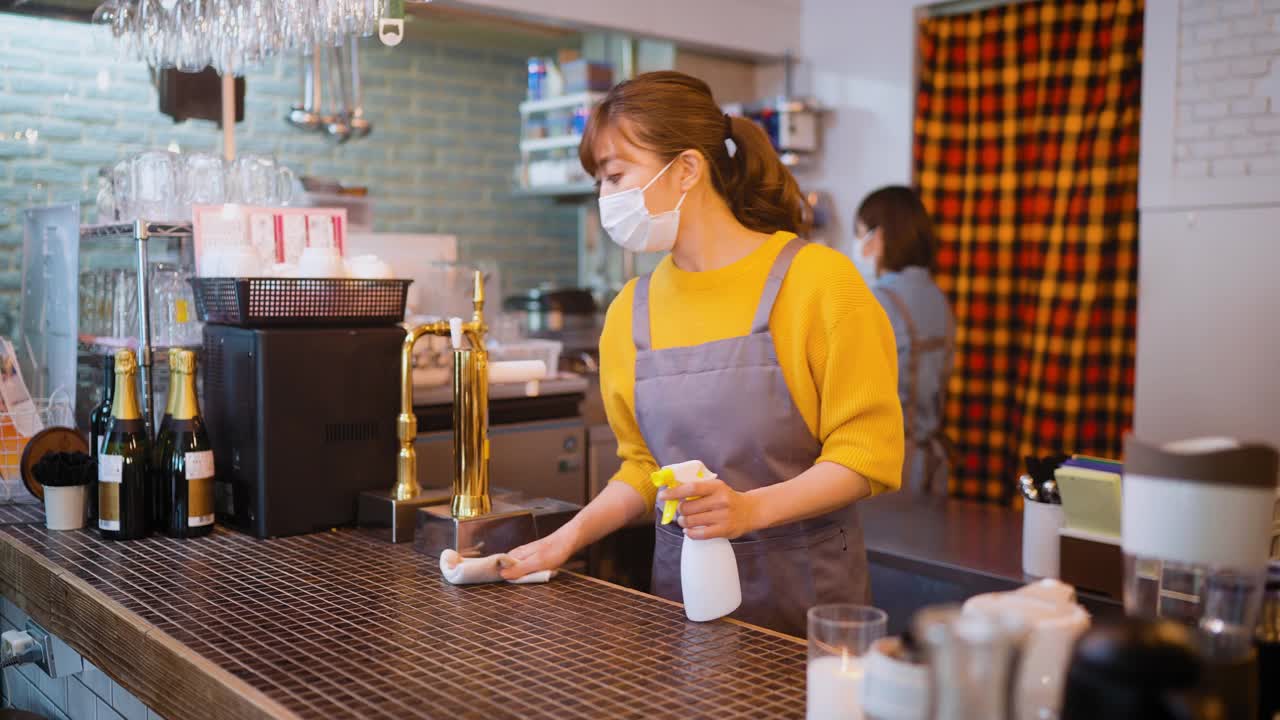 在“café”工作的两名女性戴着防护口罩，在重新开放“café”之前对桌子进行了消毒视频下载